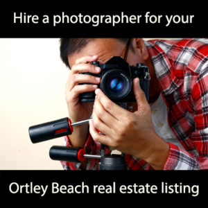 Hire a photographer for your Ortley Beach real estate listing in white font on black background with person in red plaid shirt with face hidden behind a camera on a tripod